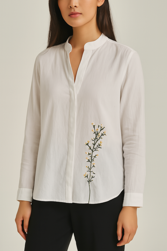 Woman wearing a white shirt with floral embroidery on a plain background